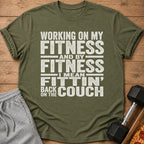 Olive green t-shirt with white text: "Working on my fitness and by fitness I mean fittin' back on the couch."