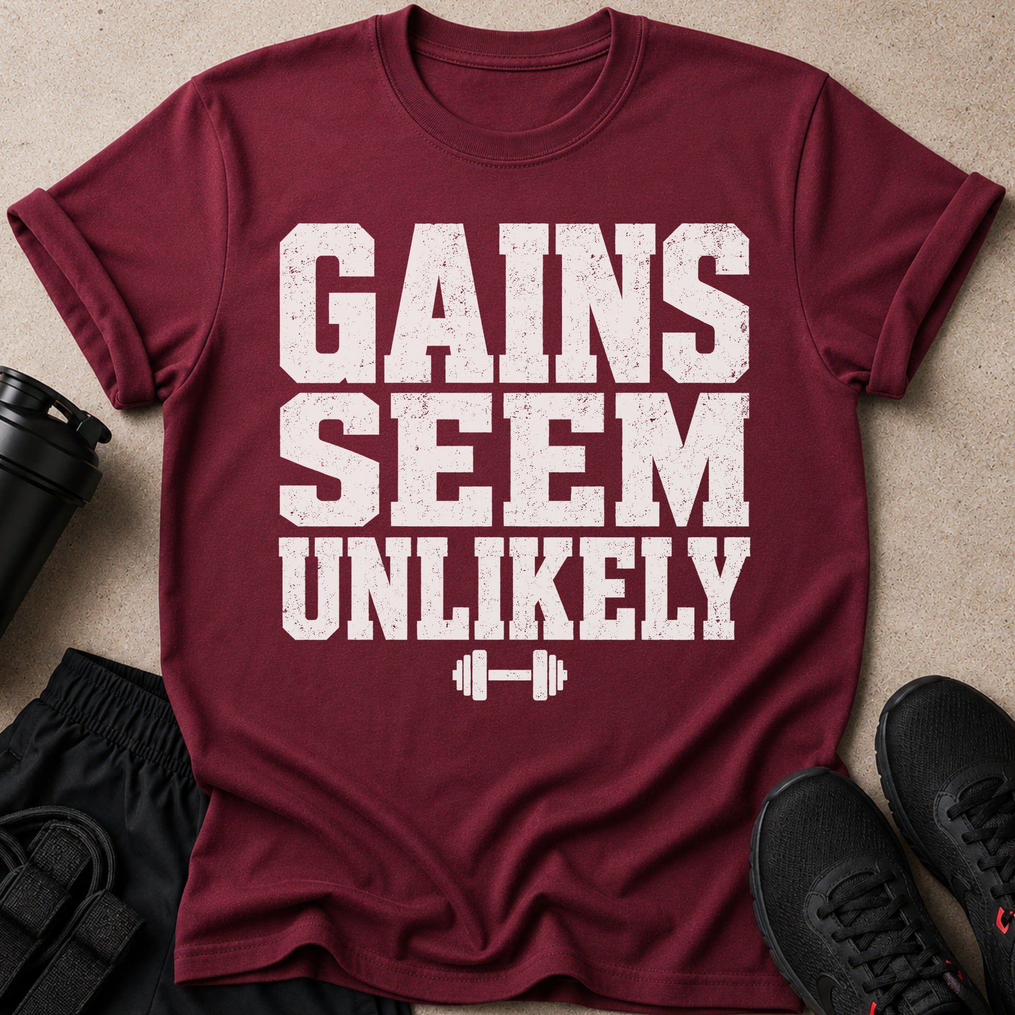 Maroon t-shirt with "GAINS SEEM UNLIKELY" text and barbell graphic.