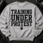 Grey crewneck sweatshirt with distressed black text "TRAINING UNDER PROTEST" and kettlebell graphic.