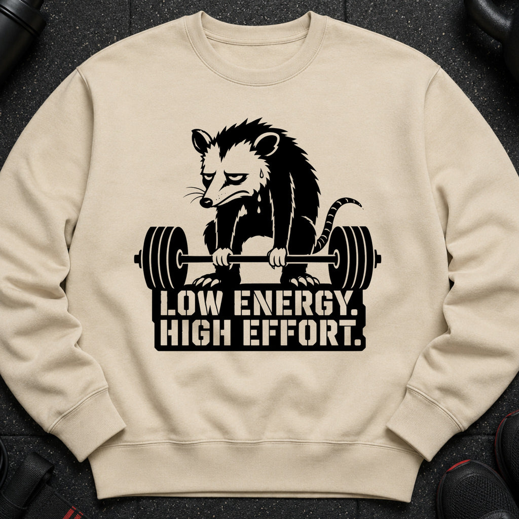 Tan sweatshirt with a black graphic of a sad opossum lifting a barbell and text.
