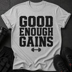 Grey t-shirt with black distressed text "GOOD ENOUGH GAINS" and barbell graphic.
