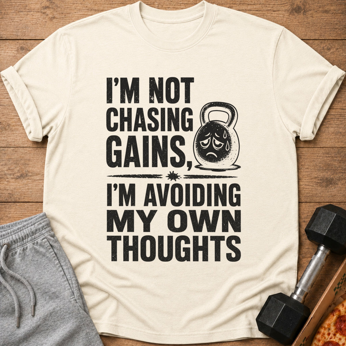Cream t-shirt with black text "I'm Not Chasing Gains, I'm Avoiding My Own Thoughts" and sad kettlebell.