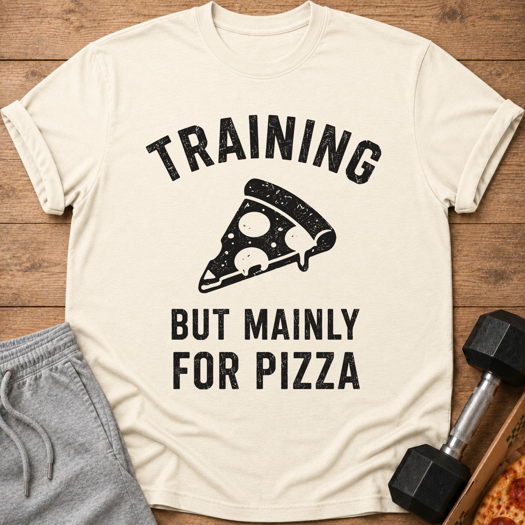 Light cream t-shirt with black text "TRAINING BUT MAINLY FOR PIZZA" and pizza graphic.