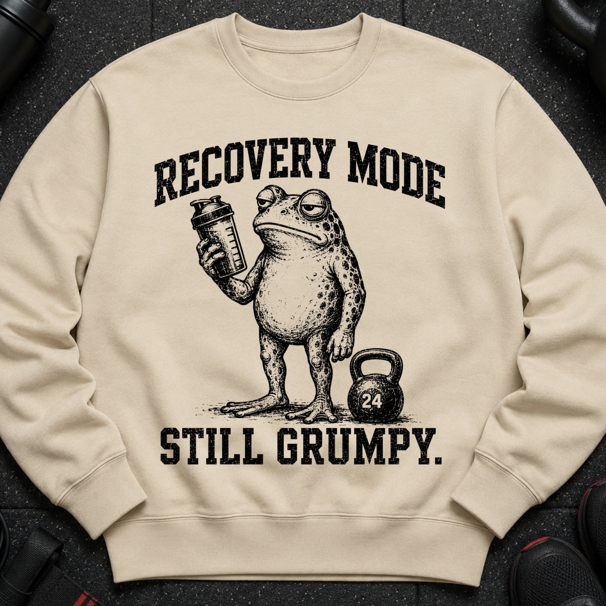 Crewneck sweatshirt with a grumpy frog holding a shaker bottle and a kettlebell. "Recovery Mode Still Grumpy."