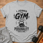 Gray t-shirt with text "I Joined the Gym for the Personality Decline" and a sad kettlebell.