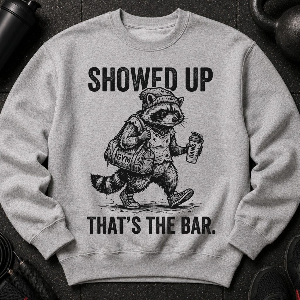 Grey sweatshirt with a black graphic of a raccoon in gym clothes holding a bag.