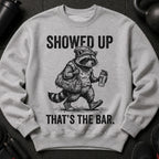 Grey sweatshirt with a black graphic of a raccoon in gym clothes holding a bag.