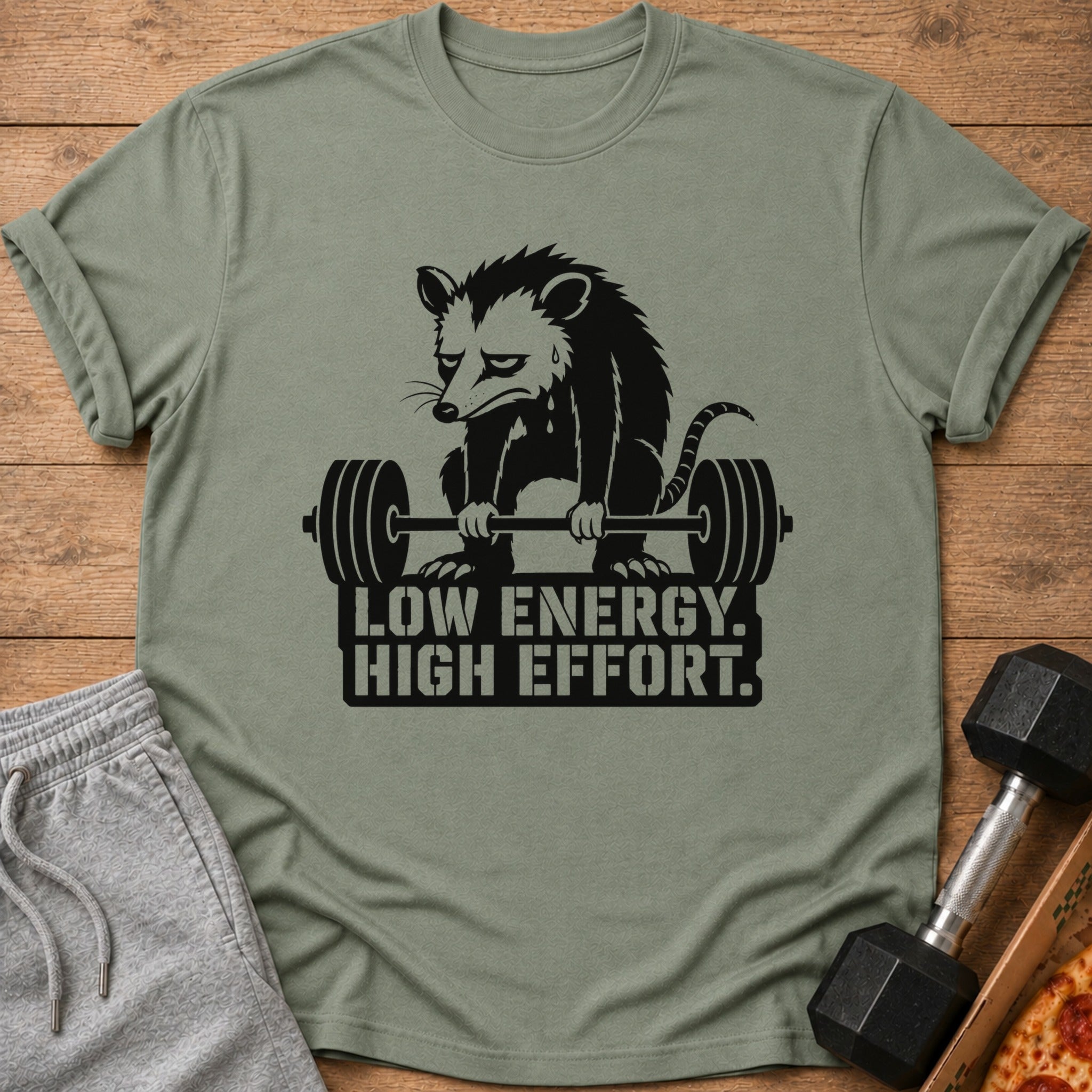 Green t-shirt with a sad opossum lifting a barbell and text "LOW ENERGY. HIGH EFFORT."