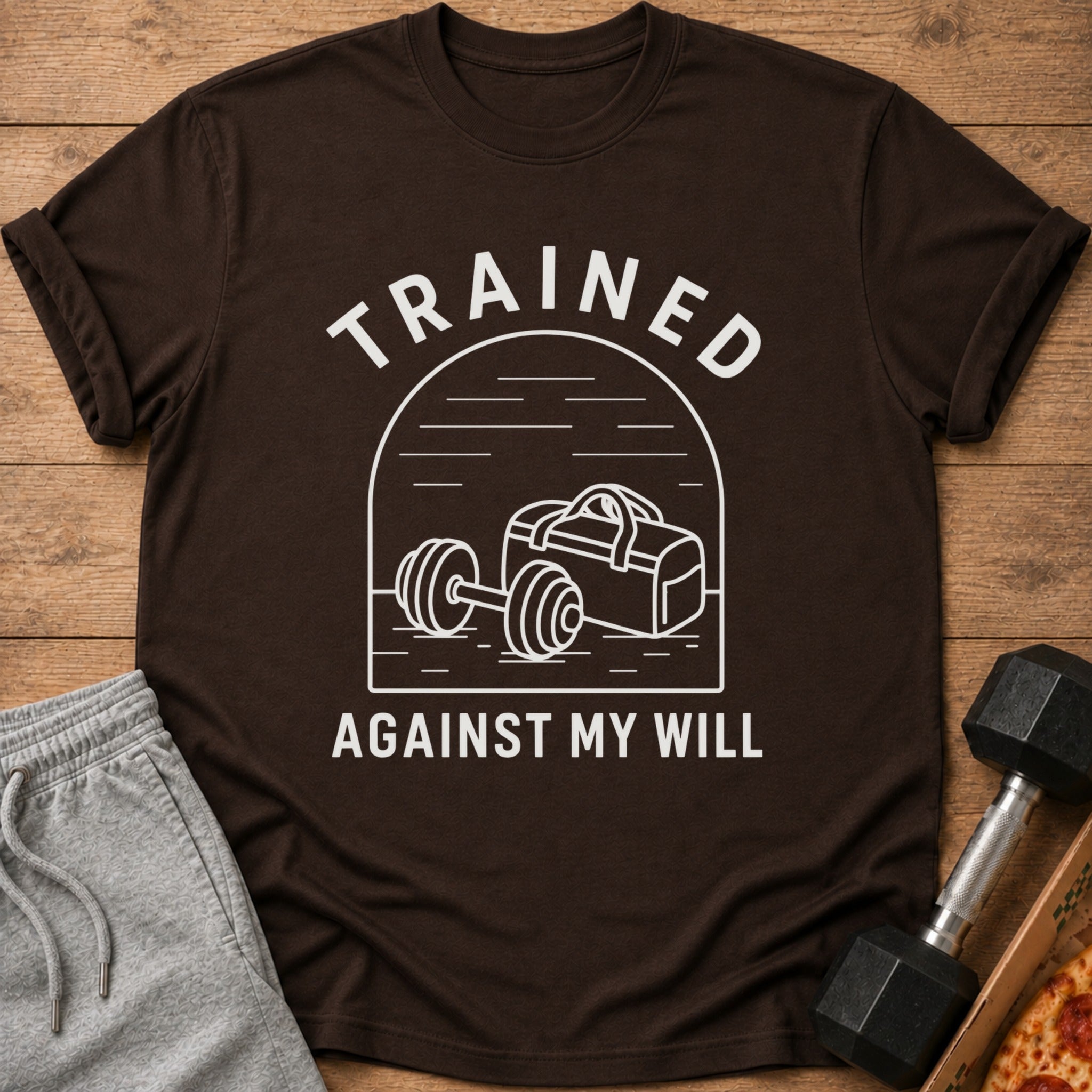 Brown t-shirt with white text "TRAINED AGAINST MY WILL" and gym graphics.