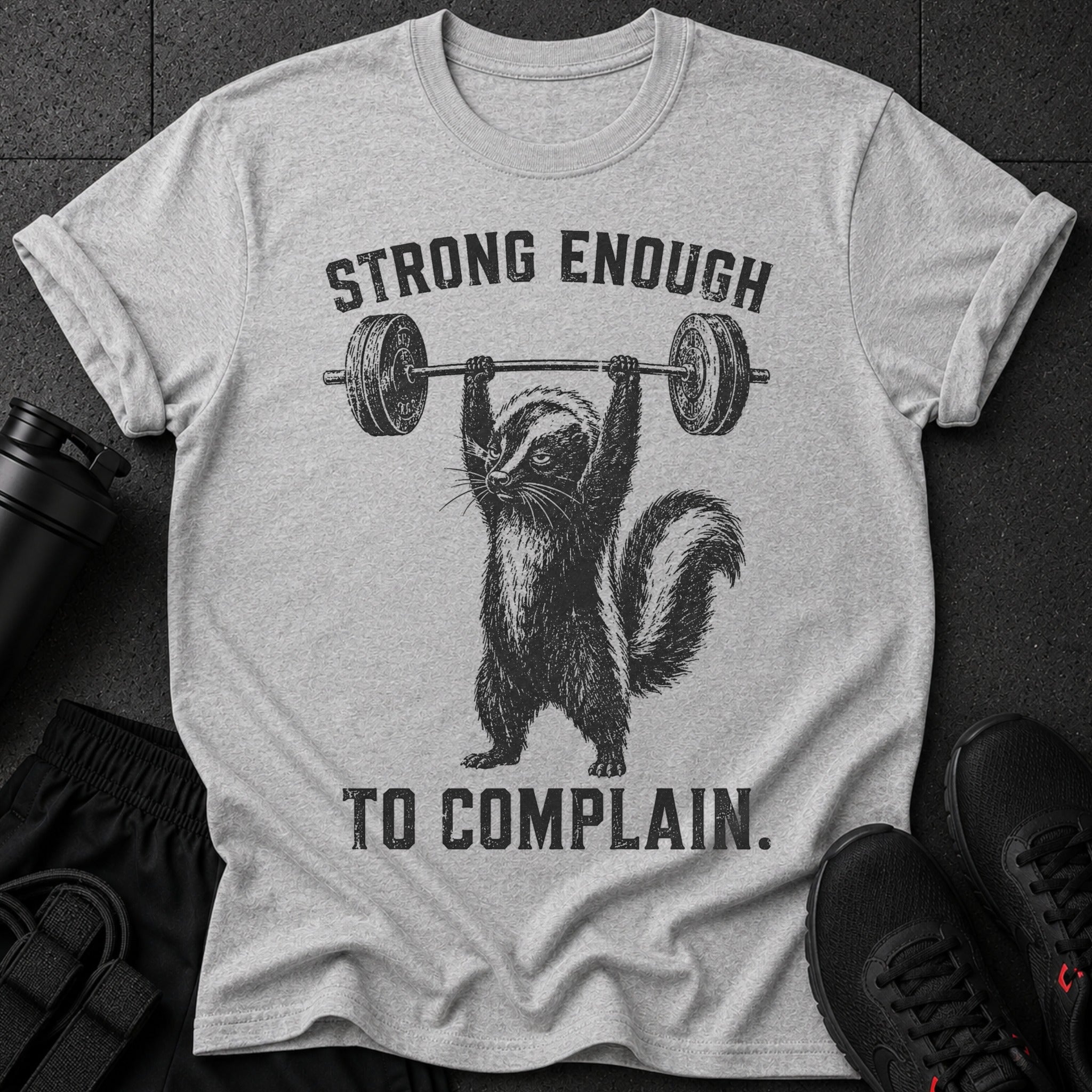 Gray t-shirt with skunk lifting barbell and text "STRONG ENOUGH TO COMPLAIN."