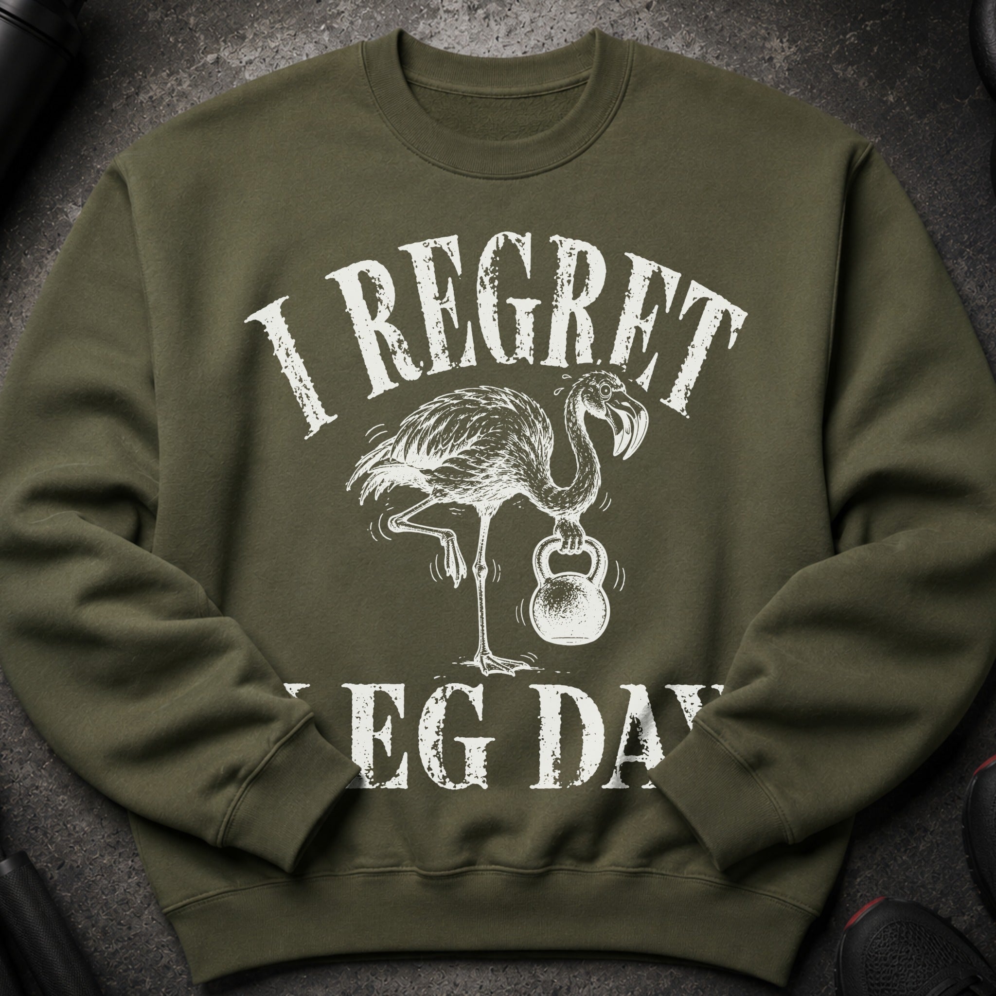 Green sweatshirt with white text "I REGRET" and a flamingo holding a kettlebell, "LEG DAY" below