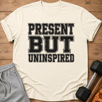 Cream t-shirt with black distressed text reading "PRESENT BUT UNINSPIRED".