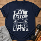 Navy t-shirt with text "LOW BATTERY. STILL LIFTING." and barbell graphic.