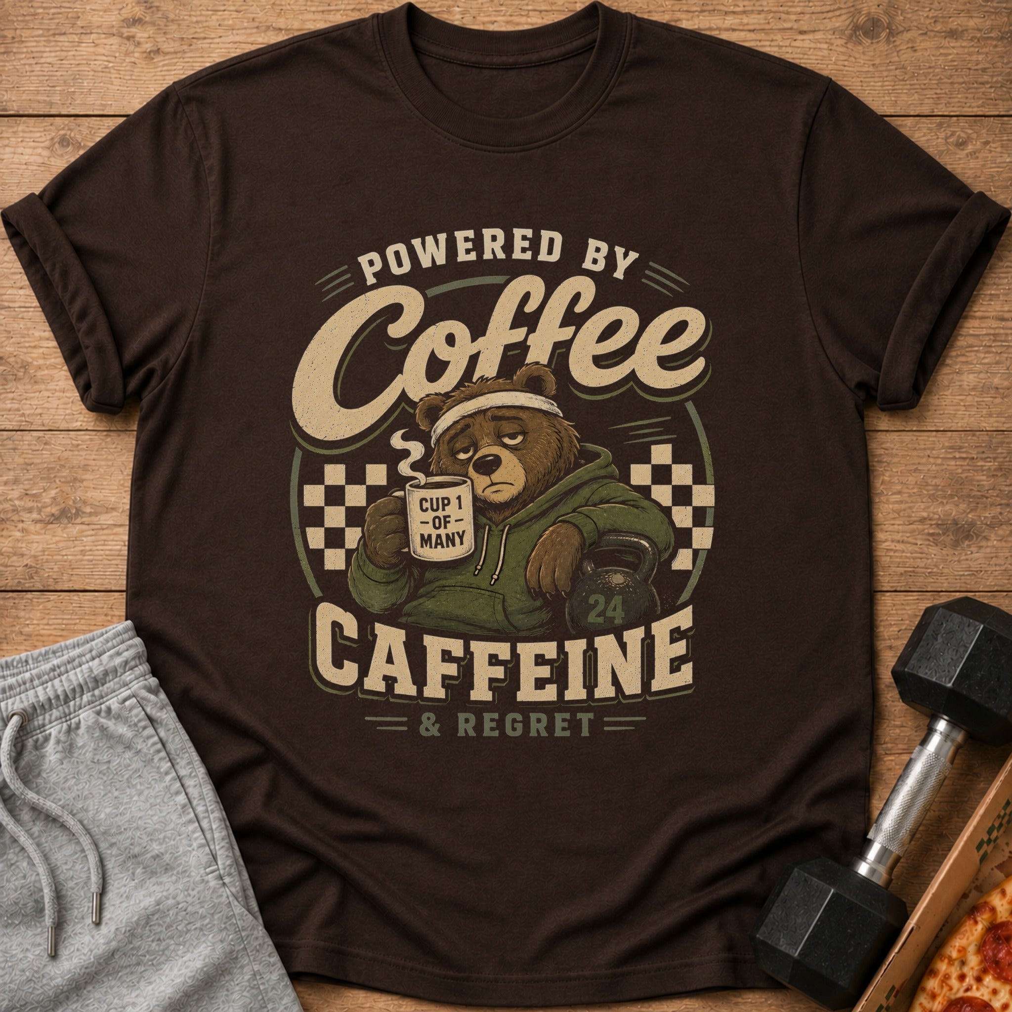 Brown t-shirt graphic: bear with coffee cup, kettlebell, and text "Powered by Coffee Caffeine & Regret".