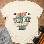 "Out of Office Out of Breath" text graphic on a tan t-shirt with suitcase and dumbbells.