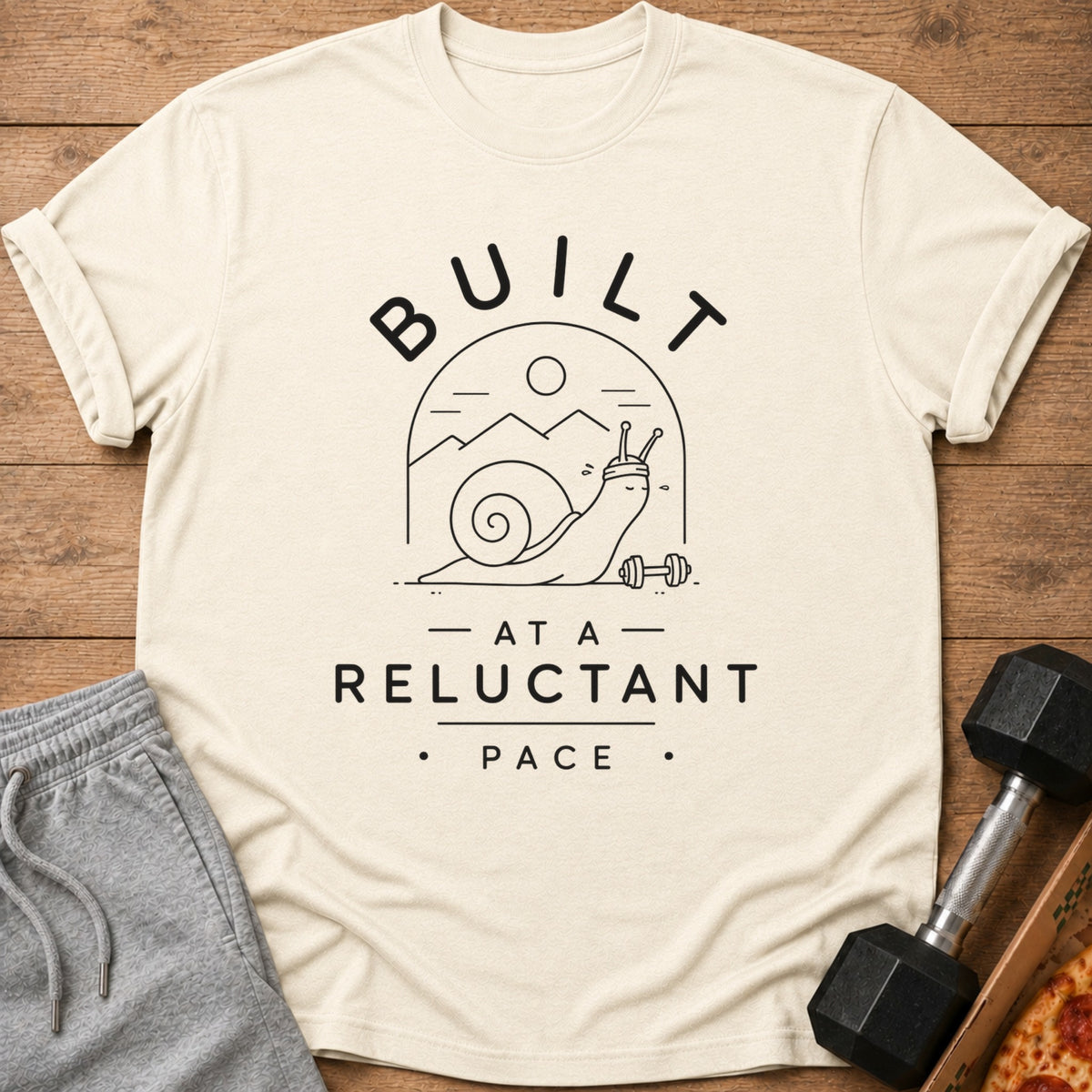 Cream t-shirt with graphic of a snail lifting weights and text "BUILT AT A RELUCTANT PACE".