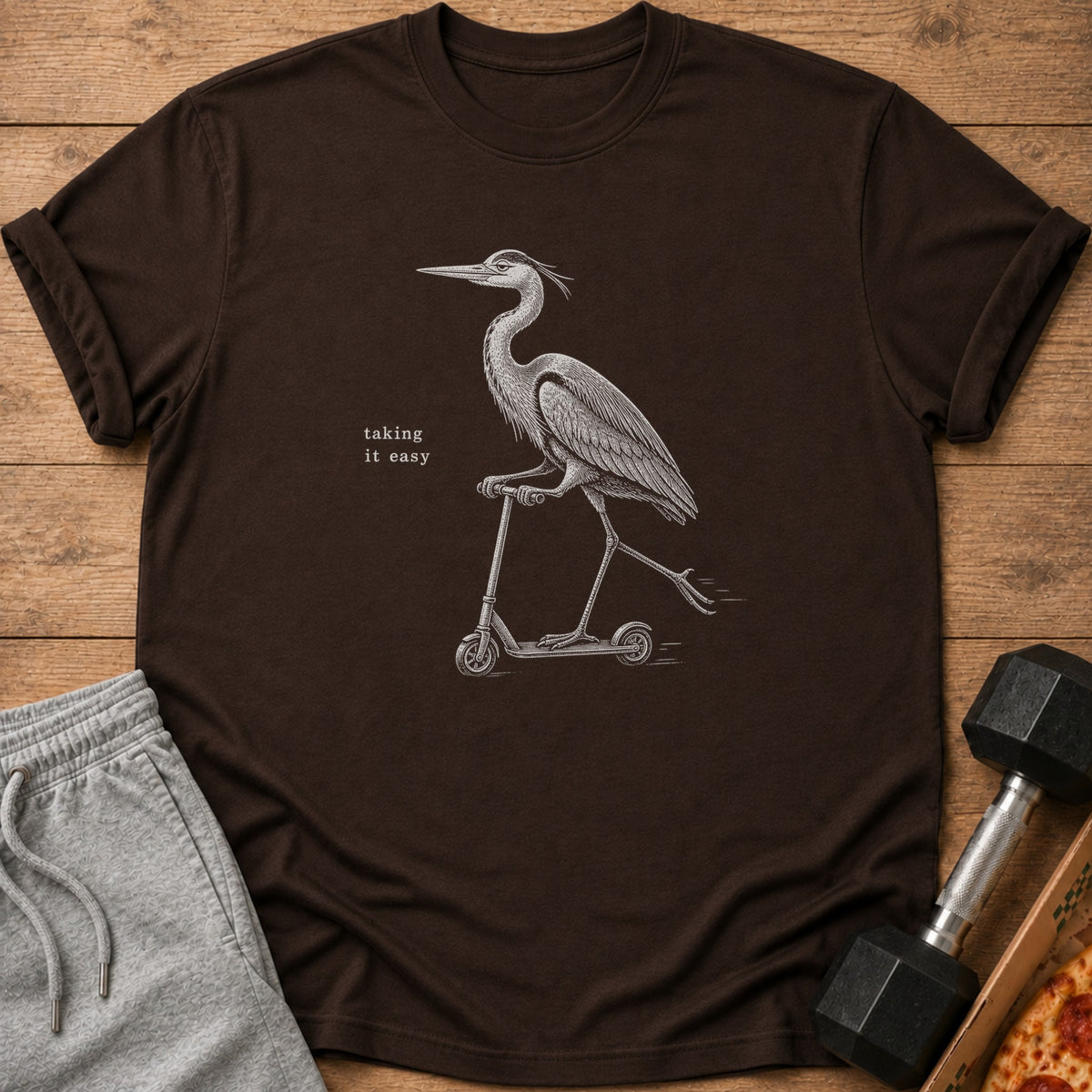 Brown t-shirt with a line drawing of a heron riding a scooter and text "taking it easy".