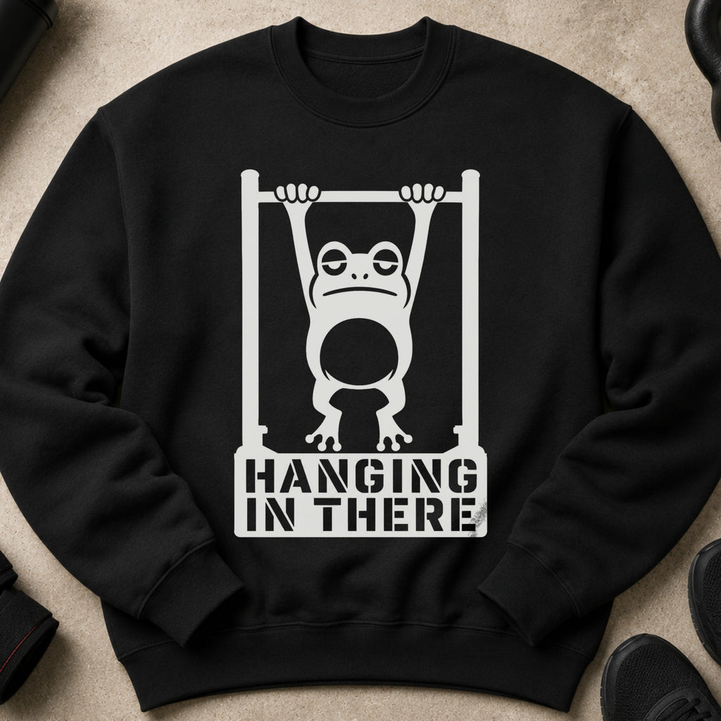 Black sweatshirt with a white graphic of a tired frog hanging from a bar, reading "HANGING IN THERE".