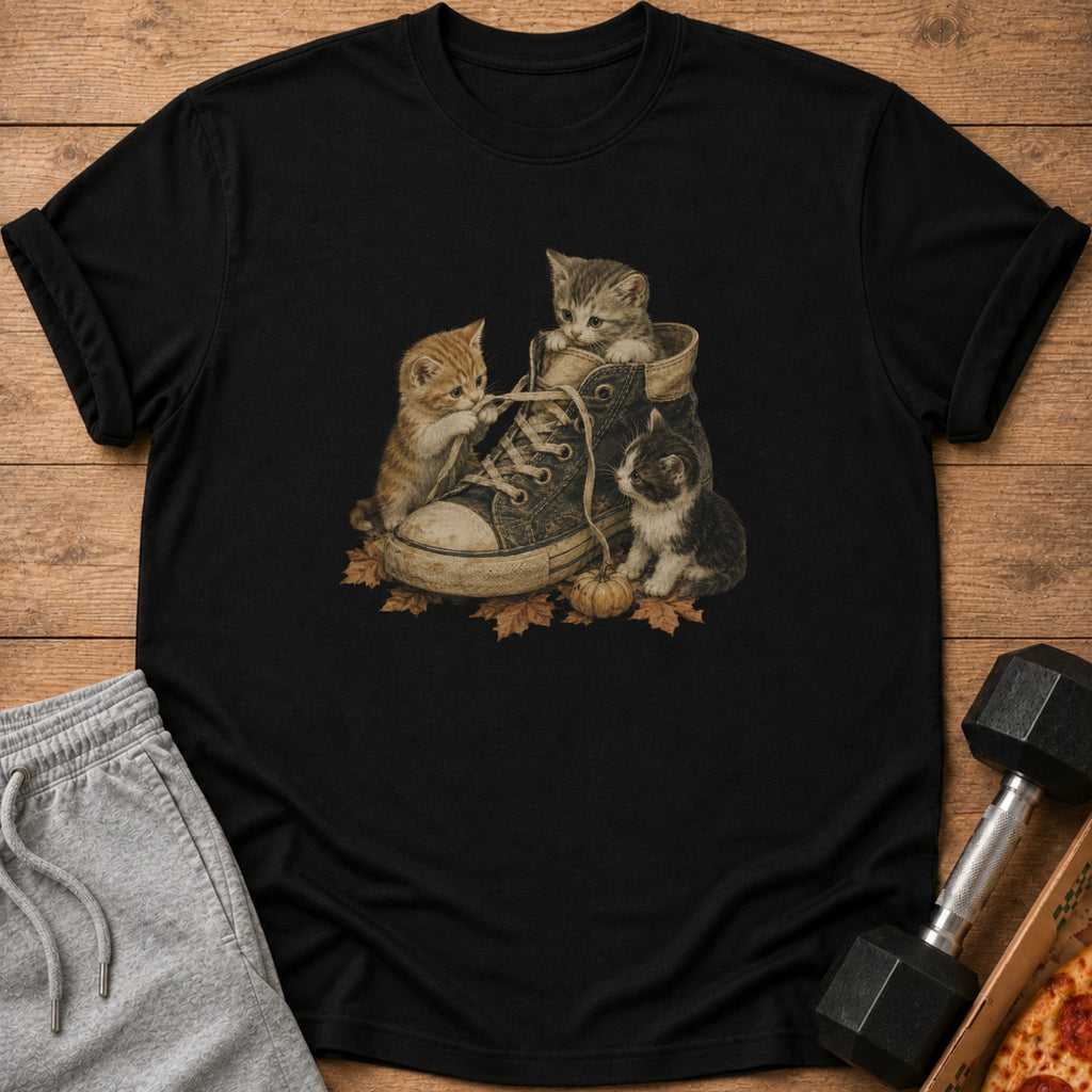 Three kittens play with the laces of a worn sneaker surrounded by autumn leaves.