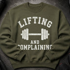 Olive green sweatshirt with white distressed text "LIFTING AND COMPLAINING" and dumbbell graphic.