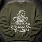 Olive green sweatshirt with opossum graphic and "Stretched Thin, Still Here" text.