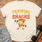 Cream t-shirt with "TRAINING FOR SNACKS" text and a cartoon pizza slice lifting dumbbells.