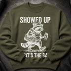 Green sweatshirt with graphic of raccoon at gym holding bag and drink.