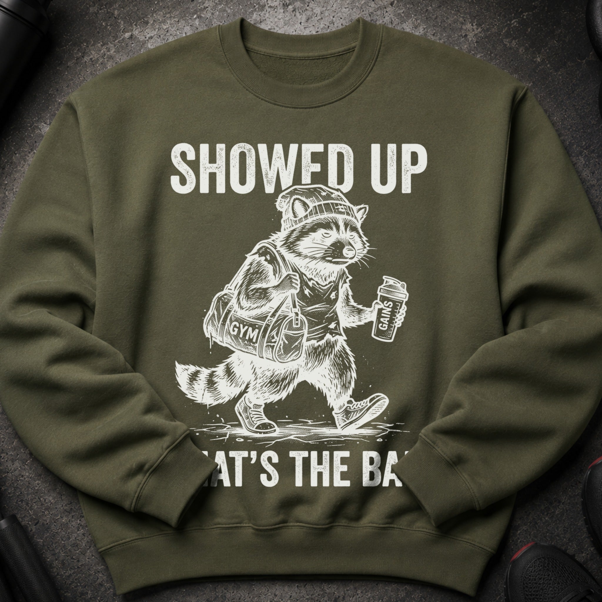 Green sweatshirt with graphic of raccoon at gym holding bag and drink.