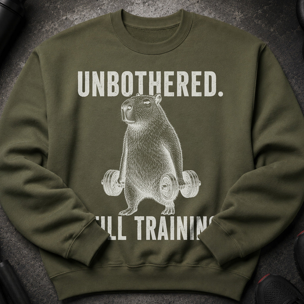 Olive green sweatshirt with "UNBOTHERED. STILL TRAINING." and a capybara lifting dumbbells.