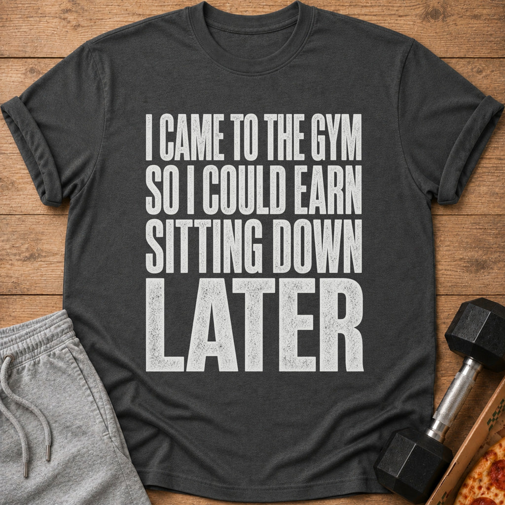 A dark gray t-shirt with white text reading "I CAME TO THE GYM SO I COULD EARN SITTING DOWN LATER".