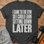 A dark gray t-shirt with white text reading "I CAME TO THE GYM SO I COULD EARN SITTING DOWN LATER".