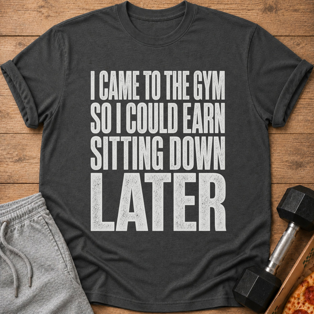A dark gray t-shirt with white text reading "I CAME TO THE GYM SO I COULD EARN SITTING DOWN LATER".