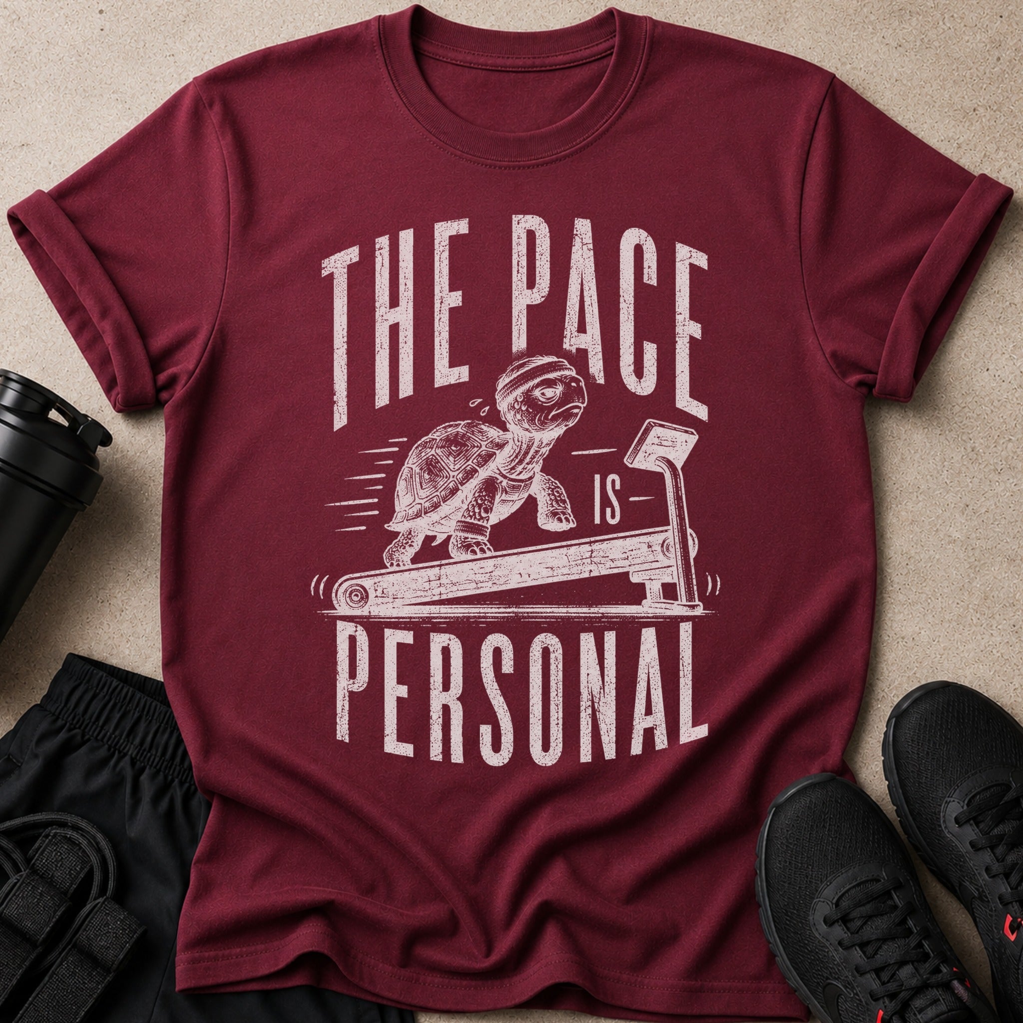 Burgundy t-shirt with turtle on treadmill graphic and text "THE PACE IS PERSONAL".