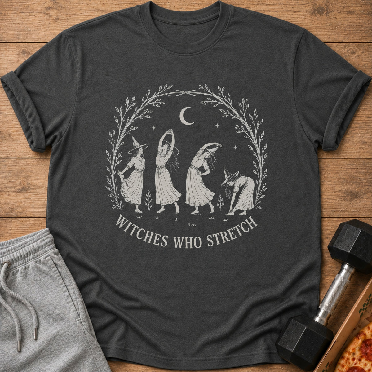 T-shirt with "Witches Who Stretch" text and four witches stretching within a leafy wreath.