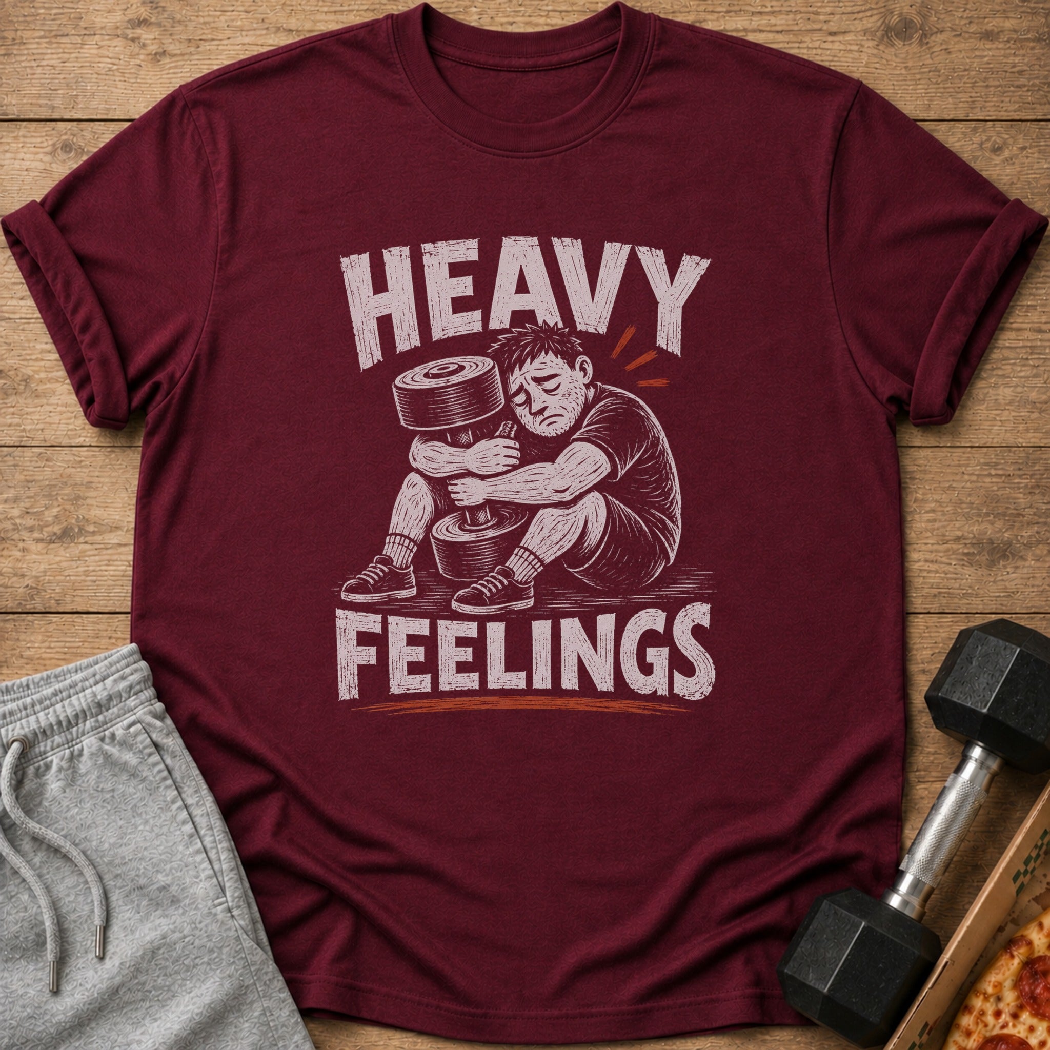 Maroon t-shirt with "HEAVY FEELINGS" text and illustration of a man hugging a dumbbell.