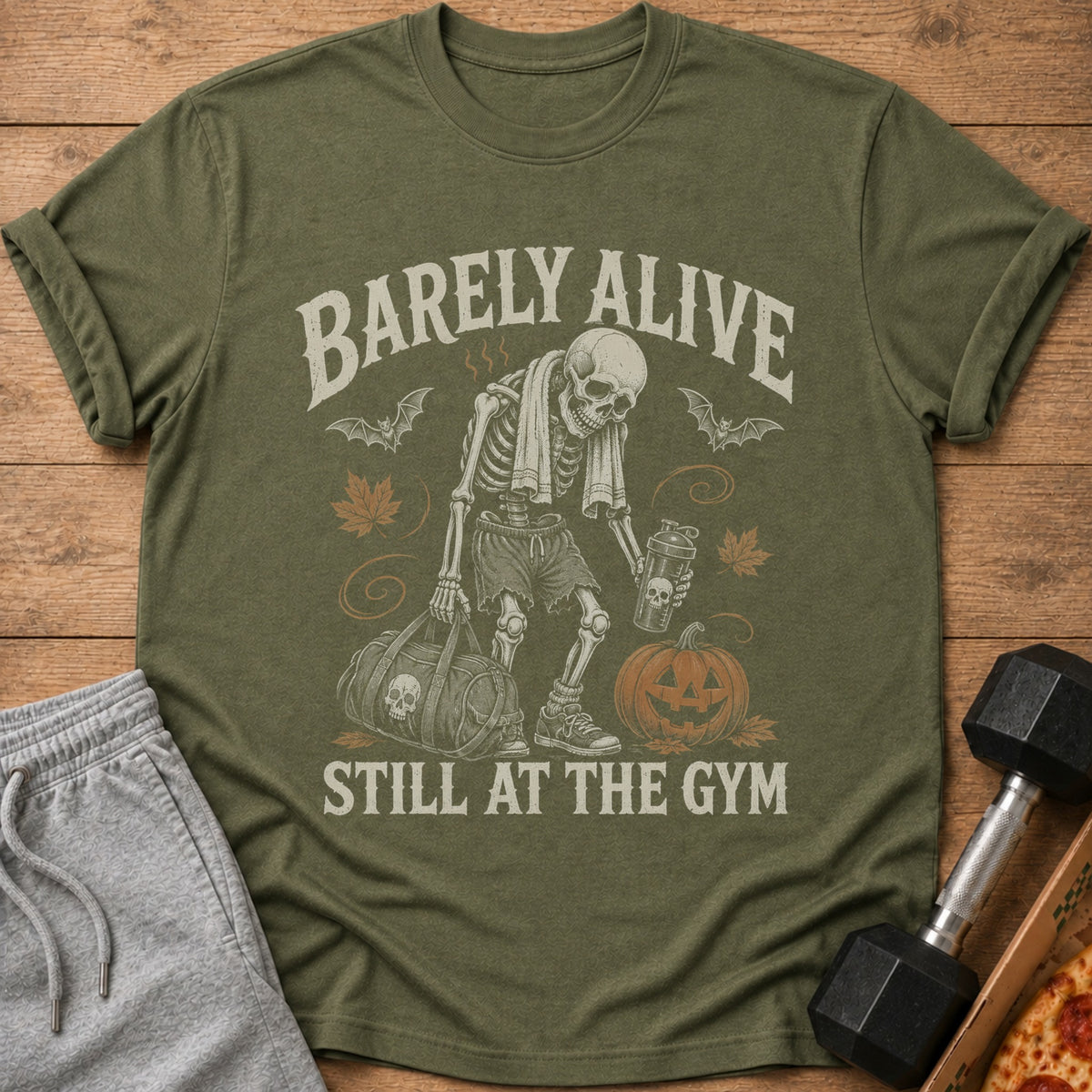 Skeleton graphic with "Barely Alive Still At The Gym" text on olive green t-shirt.