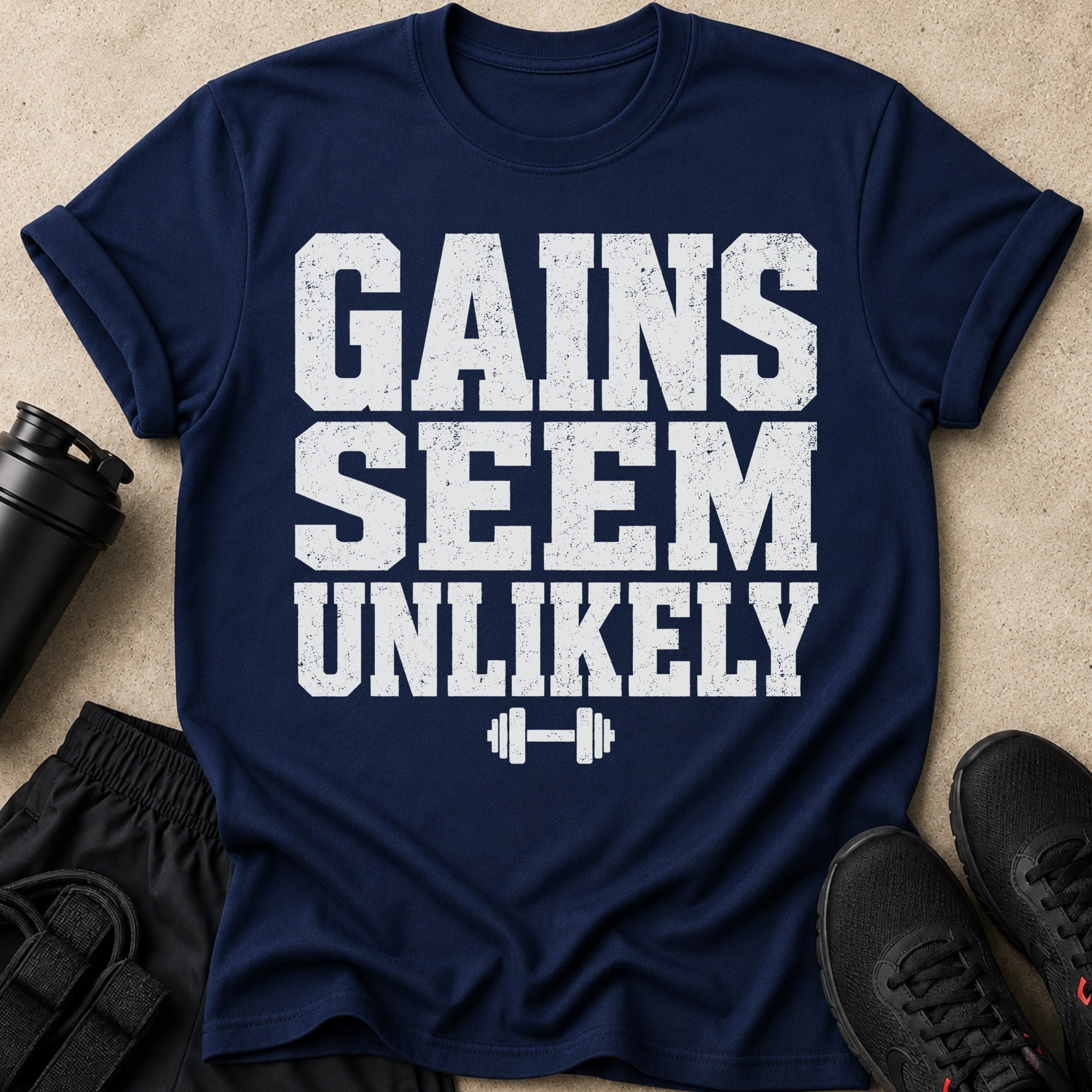 Navy t-shirt with white distressed text saying GAINS SEEM UNLIKELY and a dumbbell graphic.
