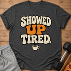Dark gray t-shirt with text "SHOWED UP TIRED" and coffee cup graphic.