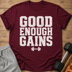 Maroon t-shirt with white distressed text "GOOD ENOUGH GAINS" and a dumbbell graphic.