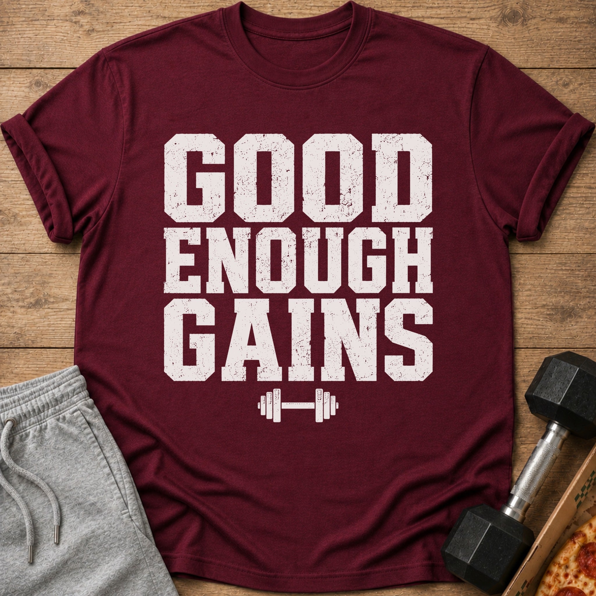 Maroon t-shirt with white distressed text "GOOD ENOUGH GAINS" and a dumbbell graphic.