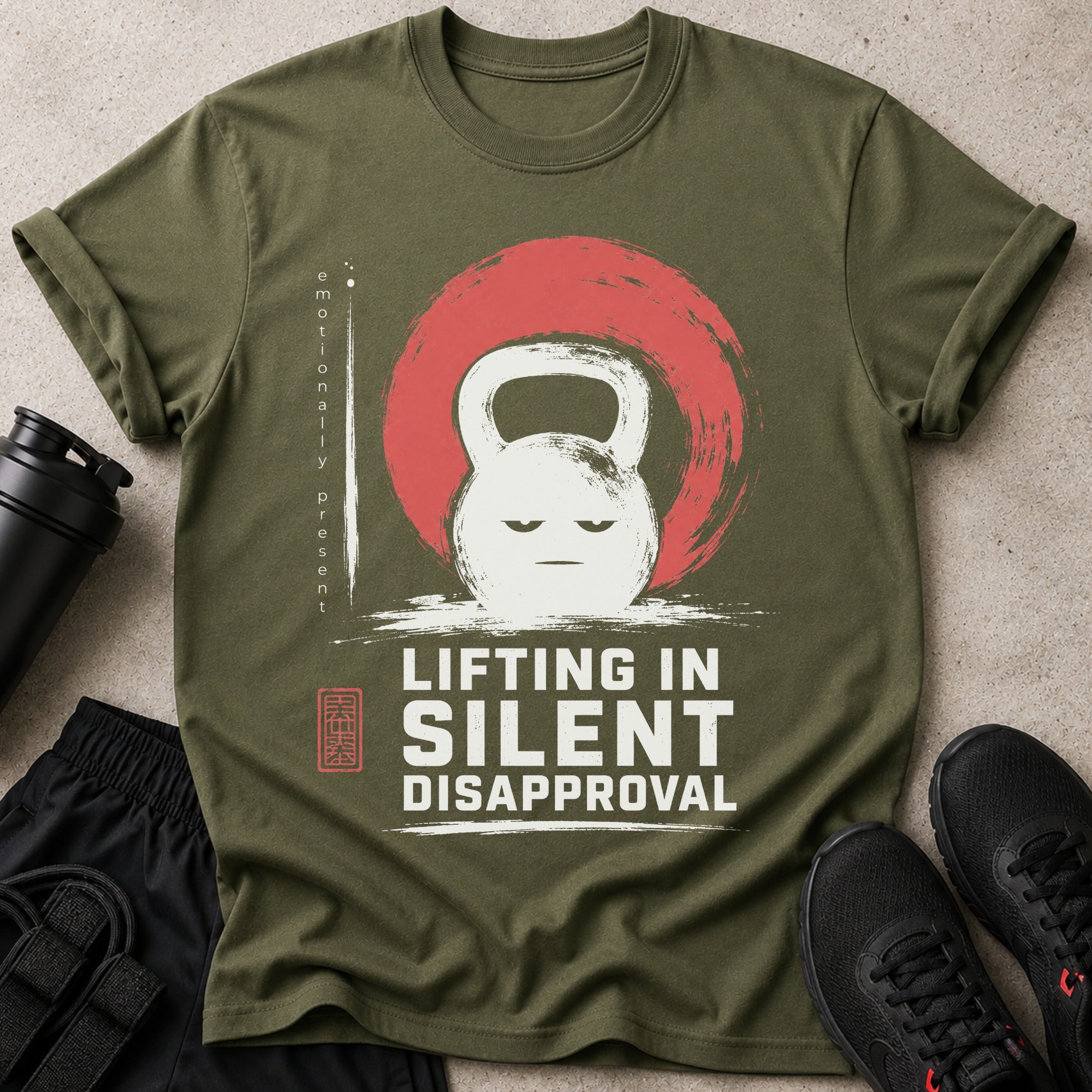 Olive green t-shirt with a grumpy kettlebell design and the text "LIFTING IN SILENT DISAPPROVAL."