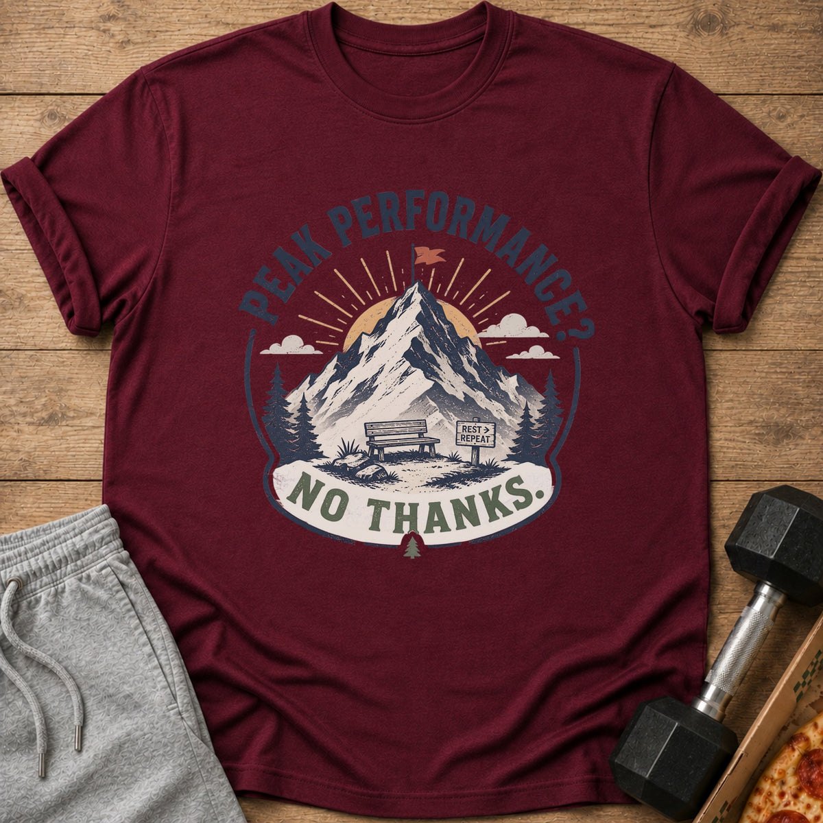 Maroon t-shirt with "Peak Performance? No Thanks." graphic featuring mountains, bench, and sign.