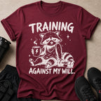Maroon t-shirt with a raccoon drinking coffee, text reads "TRAINING AGAINST MY WILL."