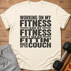 Cream t-shirt with "Working on my fitness and by fitness I mean fittin' back on the couch" text.