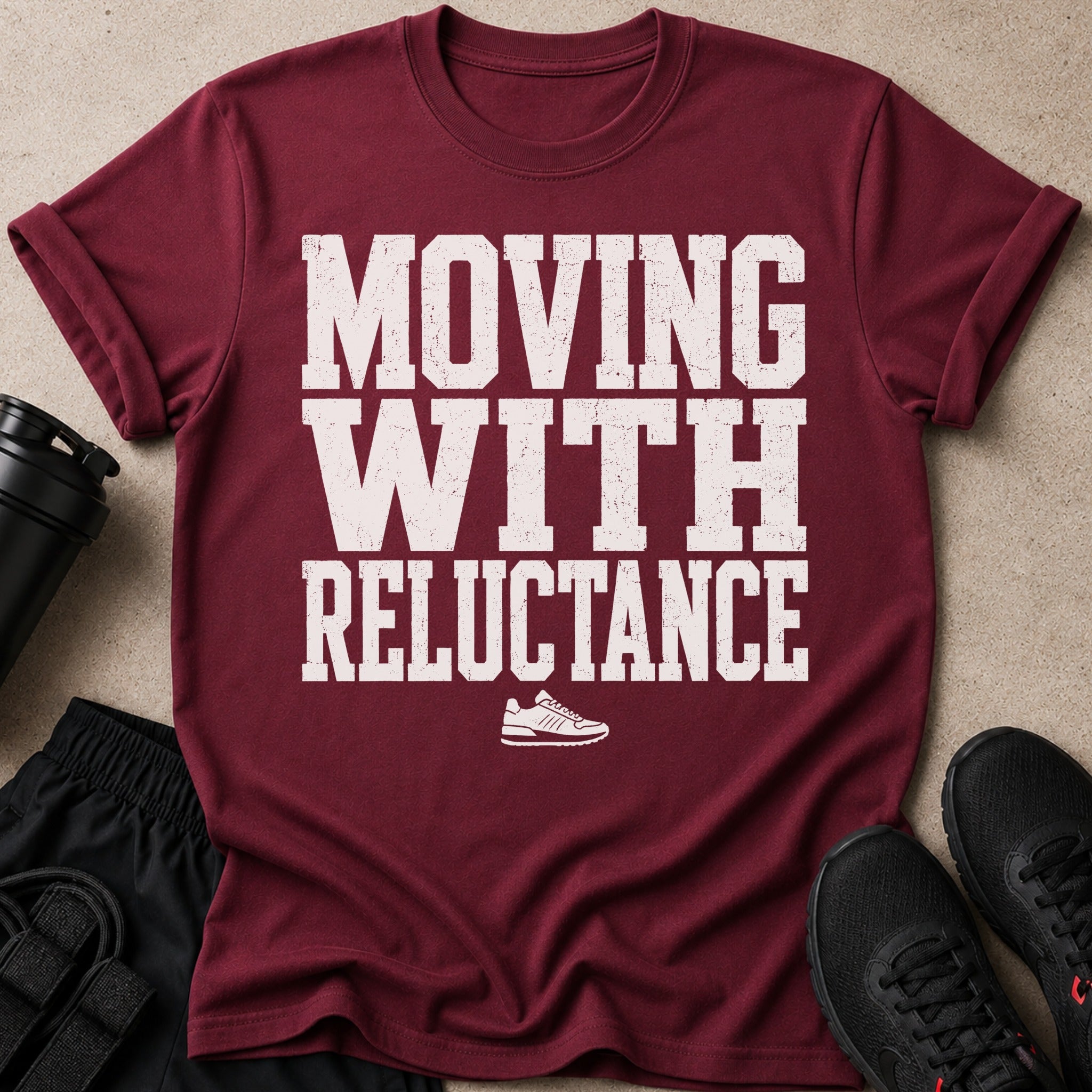 Maroon t-shirt with white text "MOVING WITH RELUCTANCE" and a sneaker graphic.