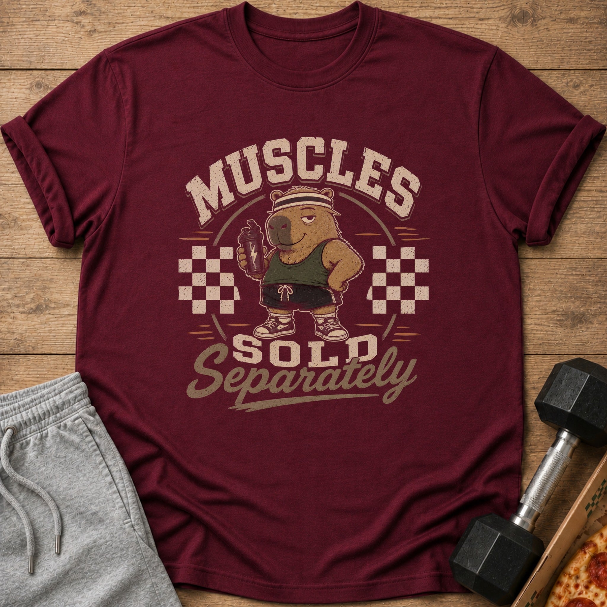 Maroon t-shirt with a cartoon capybara lifting a shaker bottle, reading "Muscles Sold Separately".