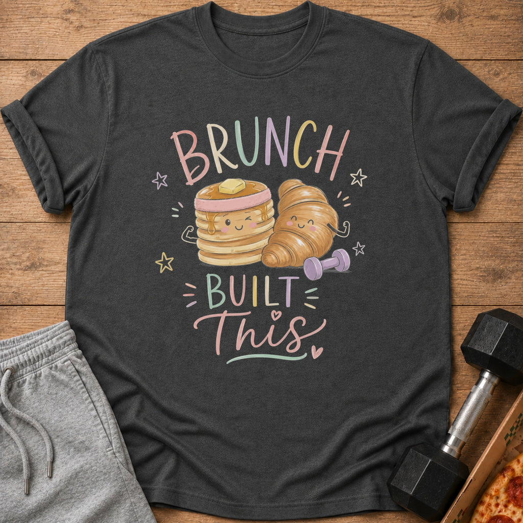 Dark gray t-shirt with a cartoon graphic featuring pancakes, a croissant, dumbbells, and the text Brunch Built This.
