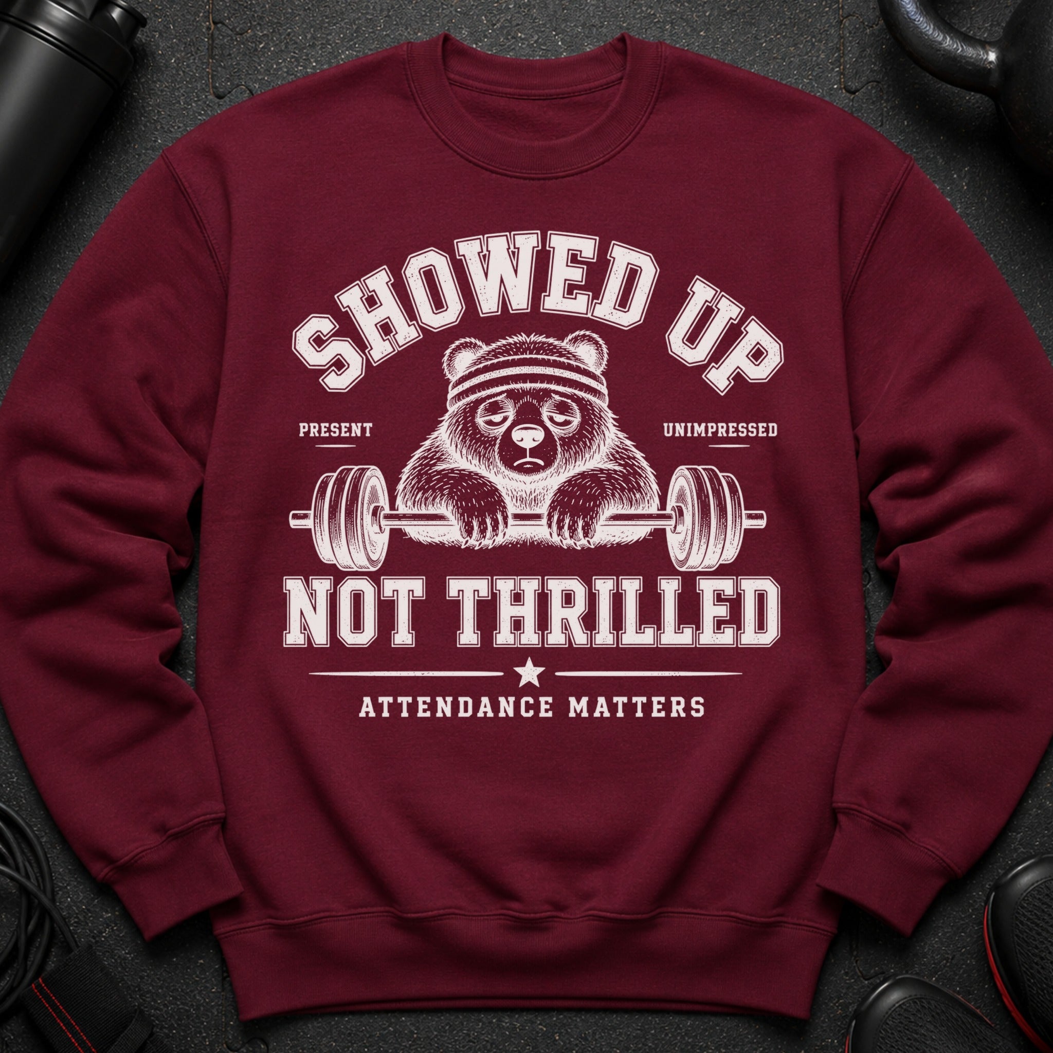 Maroon sweatshirt with a tired bear lifting a barbell, text reads "SHOWED UP. UNIMPRESSED. NOT THRILLED. ATTENDANCE MATTERS."
