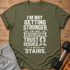 Olive green t-shirt with text: "I'm Not Getting Stronger, I'm Just Developing Trust Issues with Stairs."