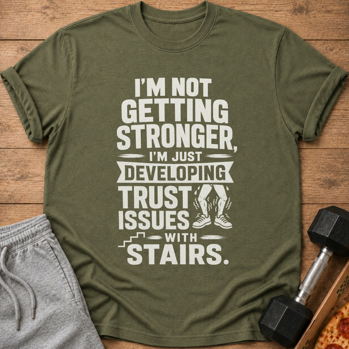 Olive green t-shirt with text: "I'm Not Getting Stronger, I'm Just Developing Trust Issues with Stairs."